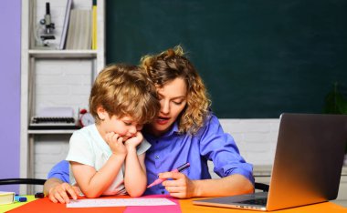 Bayan ilkokul öğretmeni tatlı öğrenciye ödevlerinde yardım ediyor. Bilgi, eğitim ve öğrenme. İlkokul öğrencisi ve özel öğretmen sınıfta aynı masada çalışıyor. Okula geri dön.
