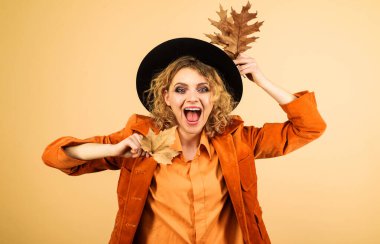 Güz yapraklı siyah şapkalı sonbahar mankeni. Sonbahar yaprağıyla şık sonbahar kıyafetleri içinde mutlu bir kadın. Sonbahar giysileri. Turuncu ceketli güzel kız ve sonbahar yapraklı şık siyah şapkalı.