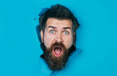 Kağıt delikten bakan sakallı adam şaşırdı. Güzel saç stili olan yakışıklı bir adam kağıt duvarda delik açıyor. Erkek kafası delikten bakıyor. Mevsimlik satış ve indirim. Reklam için boşluk kopyala