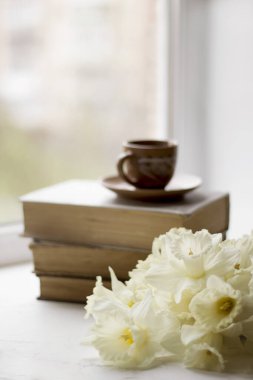 Pencere kenarında bir fincan kahve ve bahar çiçekleri olan eski kitaplar. Bir buket nergis ve ev konforu.
