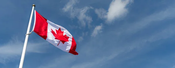 Canada Flag red maple leaf waving on a flag pole against blue sky panorama background with copy space