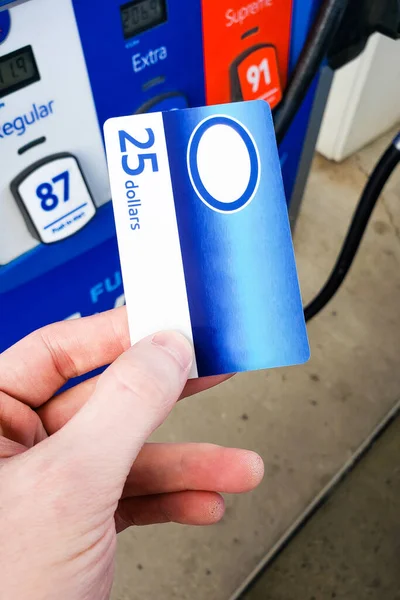 Person holding a generic gas gift card in hand and paying at the gasoline pump station. Rising gas prices and payment options