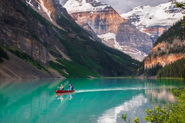 Lake Louise, Alberta, Canada - July 8 2017: Red canoe floating in turquoise water at Lake Louise. Couple canoeing together in the beautiful glacial Lake Louise at sunrise