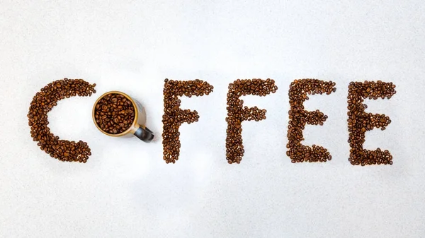 Kahve çekirdekleri ile yazılmış kelime kahve. Koyu kahve çekirdekleri yazılı olarak okunuyor. Beyaz mutfak tezgahı duvar kağıdına boşluk ve kahve metni kopyala