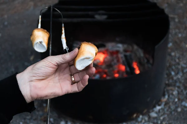 Hand roasting marshmallows on a stick over a bed of hot campfire coals. Camping and eating delicious puffy marshmallow treats