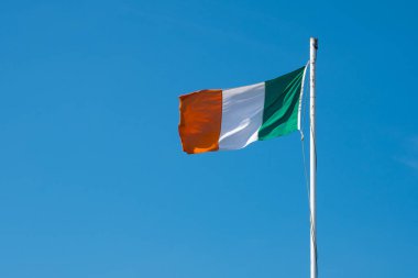 Mavi arka planda bayrak direğinde dalgalanan İrlanda bayrağı. İrlanda ulusal bayrağı direkte dalgalanıyor