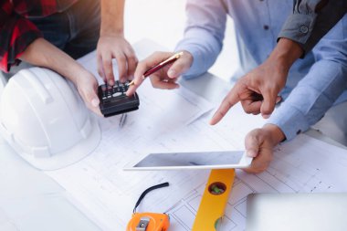 Construction concept of Engineer and Architect working at Construction Site with blue print, Engineer and Architect discussing construction plan with computer laptop calculator