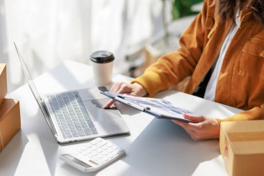 Concept of parcel delivery and selling online, Female seller or retailer using laptop to check sales of the day on online store to be packed into the parcel and ready to deliver to the customer