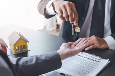 Ev satışları, ev kiralama ve emlak konsepti. Emlak acentesinin belgeleri imzaladıktan sonra ev satın alma veya kiralama sözleşmesinin şartlarını açıklarken müşteriye anahtarları vermesi