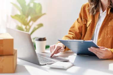 Concept of parcel delivery and selling online, Female seller or retailer using laptop to check sales of the day on online store to be packed into the parcel and ready to deliver to the customer