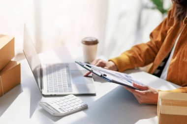 Concept of parcel delivery and selling online, Female seller or retailer using laptop to check sales of the day on online store to be packed into the parcel and ready to deliver to the customer