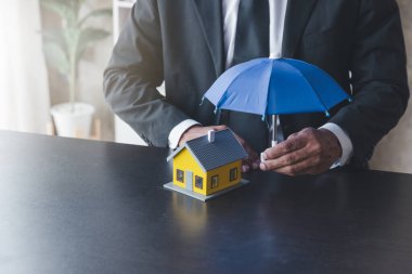 Ev sigortası kavramı. Sigorta memuru Agenen, evi korumak için şemsiye kullanıyor.