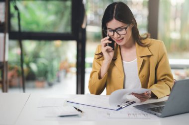 İşyeri kadınının çalışması, iş kadınının akıllı telefonu kullanması, müşterisiyle yatırım planı hakkında konuşması ve iş yerindeki belge ve iş yatırım verilerinin analiz ve kontrol edilmesi.