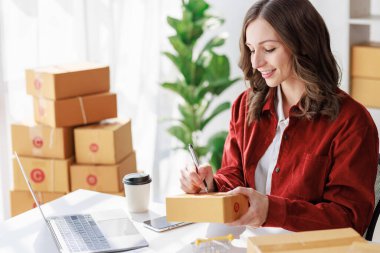 Concept of parcel delivery and selling online, Female seller or retailer using laptop to check sales of the day on online store to be packed into the parcel and ready to deliver to the customer