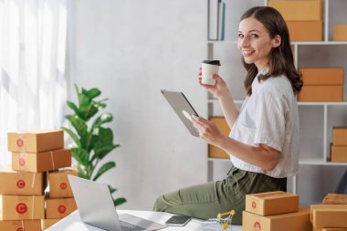 Concept of parcel delivery and selling online, Female seller or retailer using laptop to check sales of the day on online store to be packed into the parcel and ready to deliver to the customer