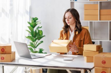 Concept of parcel delivery and selling online, Female seller or retailer using laptop to check sales of the day on online store to be packed into the parcel and ready to deliver to the customer