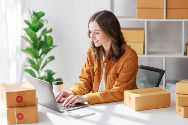 Concept of parcel delivery and selling online, Female seller or retailer using laptop to check sales of the day on online store to be packed into the parcel and ready to deliver to the customer
