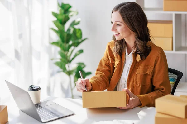 Concept of parcel delivery and selling online, Female seller or retailer using laptop to check sales of the day on online store to be packed into the parcel and ready to deliver to the customer