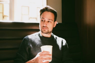 Kahve dükkanında elinde bir fincan kağıt kahve tutan bir adam.