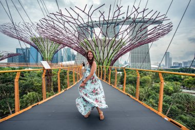 Sahildeki Singapur Bahçeleri 'nde yükseltilmiş dalgalı elbiseler içinde gülümseyen genç kadın..