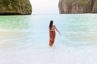 Bikinili kadın ve sarong tropik plaj cennetinde suda yürüyor. Tayland 'da yaz tatili.