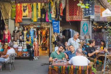 İstanbul, Türkiye - Ekim 12022: Yerel Türk erkekleri İstanbul 'daki Grand Bazaar' da renkli bir açık hava kafeteryasında geleneksel çay eşliğinde sosyalleşiyor ve sohbet ediyorlar.