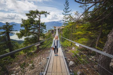 Sarışın, kadınsı bir turist, Kanadalı açık hava vahşiliğinin tadını çıkarıyor. Denizden Squamish yakınlarındaki Sky Gondola 'ya kadar asma köprü boyunca. Kanada.