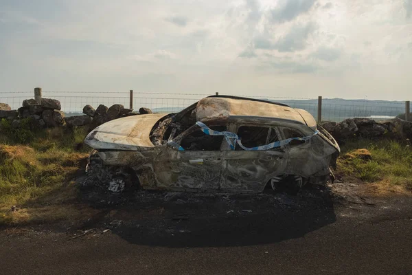 Scene of an auto accident with police tape on a burnt car wreck on a country road in the Lomond Hills Regional Park, Fife, Scotland, UK.