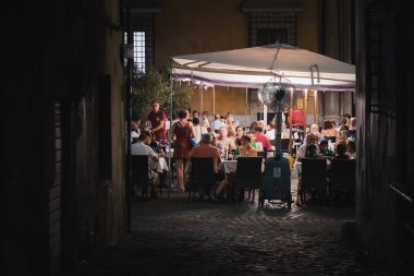 Roma, İtalya - 27 Ağustos 2023: Roma 'da müşterilerle birlikte Roma gece hayatı, Orta Roma' nın Rione VI Parione bölgesinin tarihi bir yaz gecesinde bir açık hava restoranında iklimlenmenin ve yemek yemenin keyfini çıkarmaktadır..