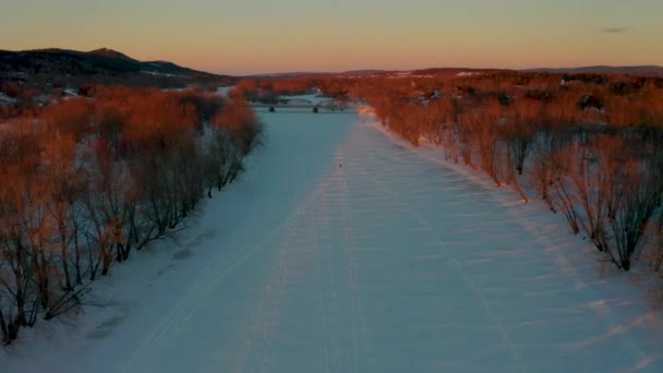 日没時に凍結した雪に覆われた川に沿って飛ぶ冬の空の景色 — ストック動画