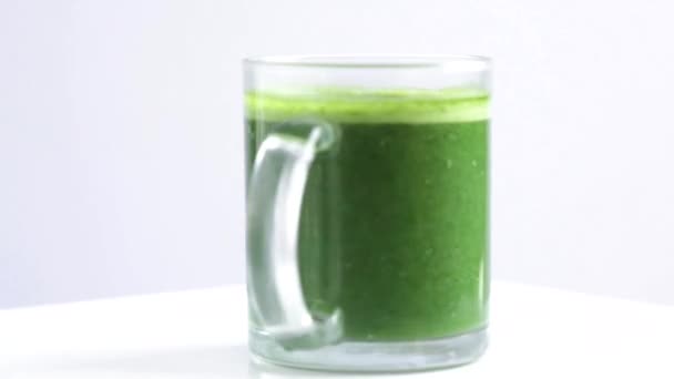 绿色苦瓜汁 在透明的玻璃杯中 有切碎的苦瓜 白色背景旋转 — 图库视频影像