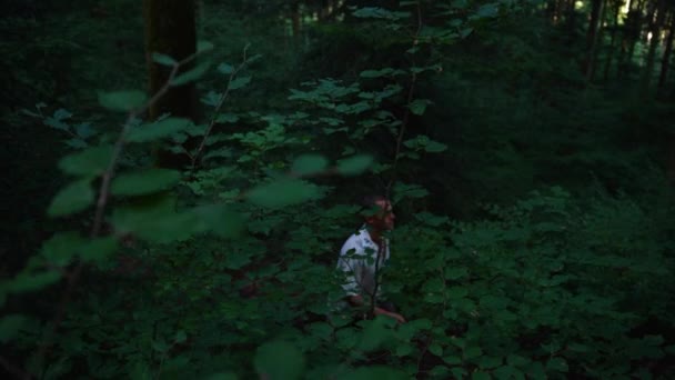 一个留着短发的年轻人在黑暗的森林里走在一条小径上 从侧面拍摄 然后跟着 — 图库视频影像
