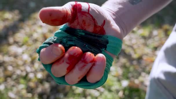 男は血を止めるために締め付けられた繊維で手を閉じ 草の背景を赤らめる — ストック動画