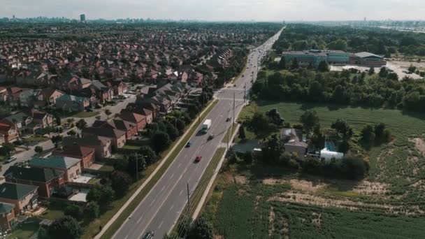 オンタリオ州の家や木がある郊外の近くで車が運転している長い道の空中ドローン映像カナダ — ストック動画