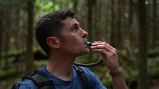 一个背包客从他的水合物袋中喝水 他惊叹于森林中周围环境的美丽 — 图库视频影像