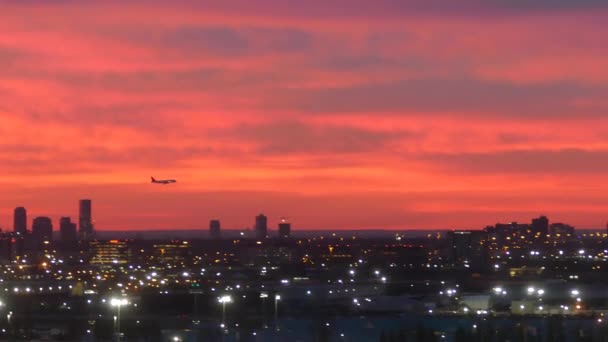 Силуэт Посадки Самолета Над Городским Пейзажем Сияющими Огнями Красным Закатом — стоковое видео