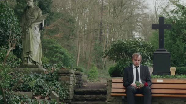 悲伤的男子坐在墓地的长椅上 — 图库视频影像