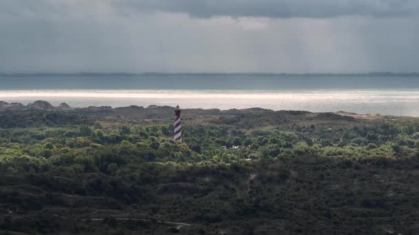 赤と白の縞模様の灯台塔の空中周回ビュー雨や雲が圧延で海岸を見下ろすドレスから突き出ています — ストック動画