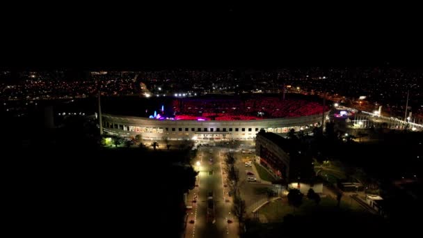 コールドプレイコンサート カラフルな光のショーの間にフルパックされたスタジアムに向かって飛ぶドローン — ストック動画