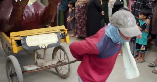 インドネシアの芸術文化のカーニバルに地元の人々が乗る紙で作られたレプリカ車を引く男 — ストック動画