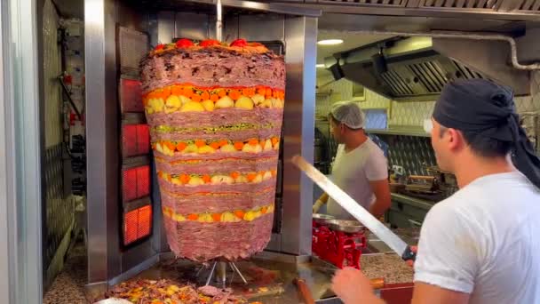 トルコのボドルムにあるケバブレストランで垂直ロティスリーから肉を切る男 キッチンで働く人々 おいしい伝統的な食べ物 棒の上にジャガイモとニンジンで味付け肉 4Kショット — ストック動画