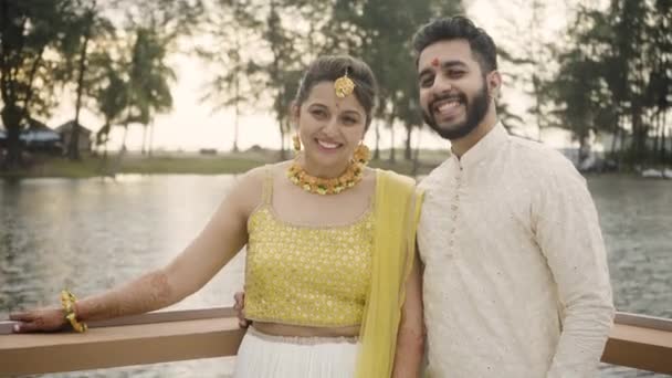 迷人的印度新娘和新郎在相机前微笑 在他们的婚礼周内举行的哈尔迪仪式上拍摄海滨和树木背景的照片 中等程度的衣服 — 图库视频影像