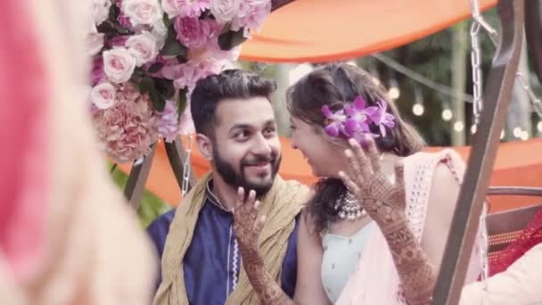 美丽的印度新娘和新郎坐在新娘的婚纱上 一边微笑着 一边戏弄对方 一边在他们的婚礼周期间在Mehndi的宴会上拍照 中等程度的衣服 — 图库视频影像