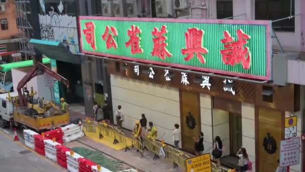 中国人の歩行者は 道路の修理と作業を継続するために 建設労働者が障壁を設定すると 上に大きなネオンサインのビジネスを過ぎて歩く — ストック動画