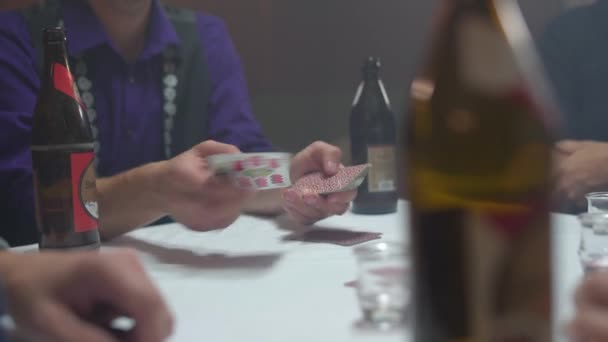 漠然とした部屋で前景にビールのボトルを持つ他のプレイヤーにカードを配布手でチロルカードゲームをプレイ男性のグループの閉鎖 4Kで撮影 — ストック動画