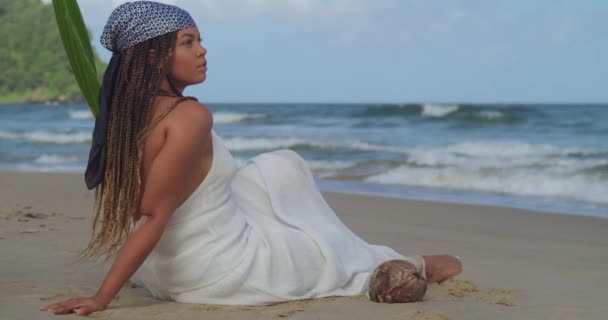 美丽的年轻女子坐在沙滩上 看着身后的海浪 — 图库视频影像