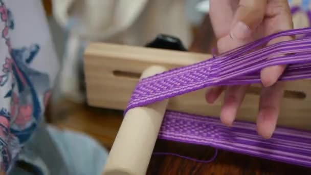 古代の木製の織物装置で伝統的なアジアのベルトに織り込まれている紫と白の糸は 終わりの時の経過として撮影 — ストック動画