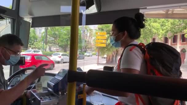 バスの運転手には バスの切符を払っている 人々はスペインのバスに乗って顔のマスクを着ています 車はバスの外の通りに停まっている 女が運転手に金を払ってる — ストック動画