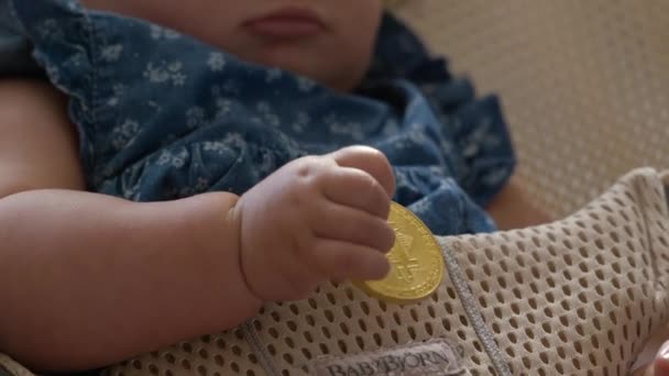 彼女の椅子に揺られている間にビットコインを持っているかわいい赤ちゃんは 手とビットコインで閉じます — ストック動画