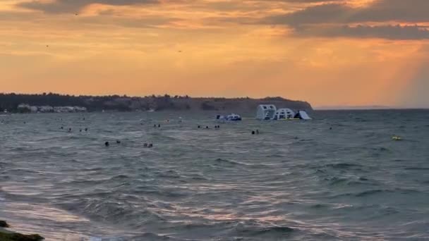 Pessoas Nadando Mar Ondulado Castelo Insuflável Pôr Sol Dourado Fundo — Vídeo de Stock